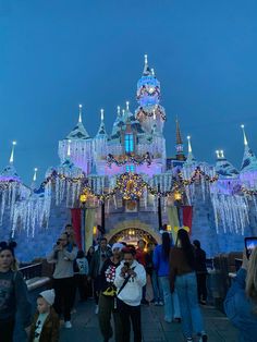 people are standing in front of a castle with lights and snow on the walls at night