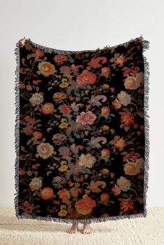 a black floral tapestry with fringes hanging on a wall next to a pair of sandals