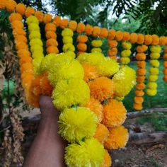 a hand is holding yellow and orange pom - poms in front of some trees