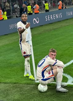 two soccer players are sitting on the field with their arms around each other as they look down