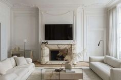 a living room with white furniture and a flat screen tv mounted on the wall above a fireplace