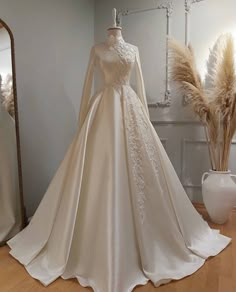 a white wedding dress on display in front of a mirror and vase with dried flowers