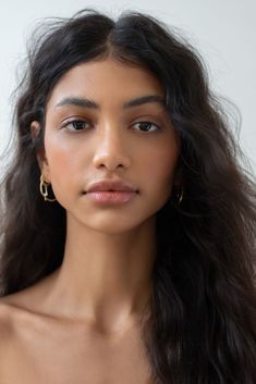 a woman with long dark hair wearing gold hoop earrings on her head and looking off to the side