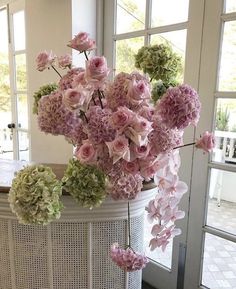 a vase filled with lots of pink and green flowers on top of a white table