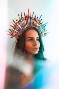 a woman with colored pencils on her head is looking at the camera while she stands in front of a mirror