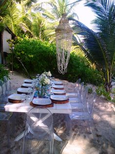 the table is set with plates and place settings for dinner on the beach, surrounded by palm trees