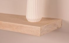 a white vase sitting on top of a wooden shelf next to a wall light fixture