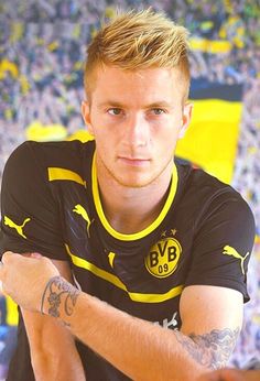 a man with tattoos sitting in front of a stadium full of people looking at the camera