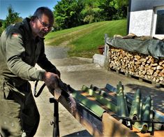 a man is working on some kind of metal item in front of a pile of firewood