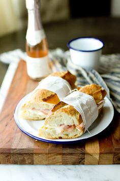 two sandwiches wrapped in white paper on a plate next to a cup and saucer