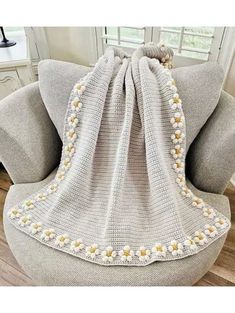 a crocheted blanket sitting on top of a gray chair next to a window