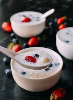 two bowls filled with yogurt and strawberries on top of a black table