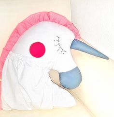 a white pillow with a pink and blue bird on it's face, sitting on a couch