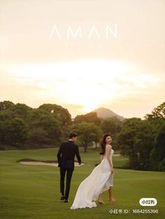 a man and woman walking across a lush green field with the sun setting behind them