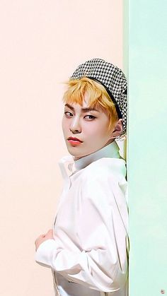 a woman with blonde hair wearing a white shirt and black checkered headband leaning against a wall