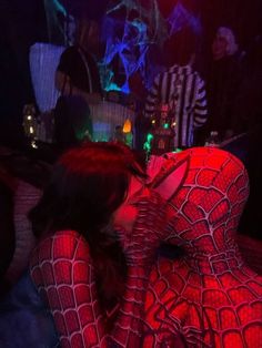 a woman in a red spider suit is kissing her man on the cheek at night