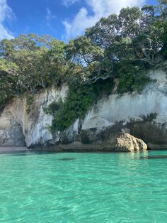 the water is crystal blue and clear with trees growing on the cliff side behind it