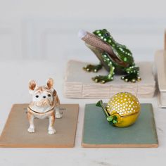 small figurines are sitting on coasters next to a frog and a lemon