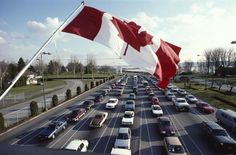 the canadian flag is flying high over a busy highway filled with cars on both sides