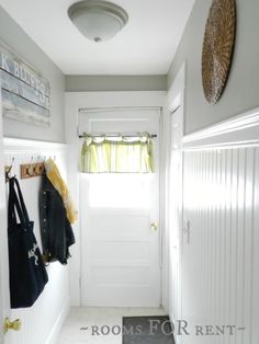 a white hallway with coat racks and coats hanging on the wall, next to a door