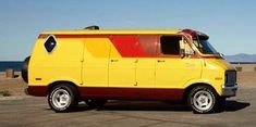 a yellow van is parked in the parking lot near the water and sand, with mountains in the background