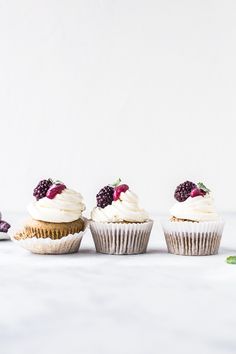 three cupcakes with white frosting and raspberries are lined up on a table