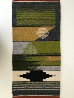 a multicolored rug hanging on a wall with a black object in the middle