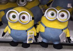 two yellow and blue minion stuffed animals are in a store shelf with other plush toys behind them