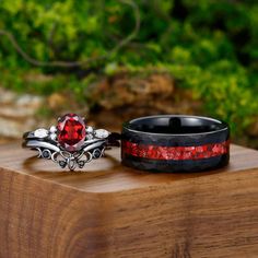 two wedding bands with red and black stones on them sitting on a wooden surface next to each other