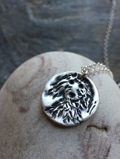 a silver necklace with a tree on it sitting on top of a stone slab next to a rock