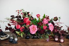 a wooden table topped with vases filled with flowers and berries next to candles on top of it