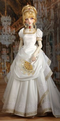 a doll in a white dress with gold trimmings and a golden brooch