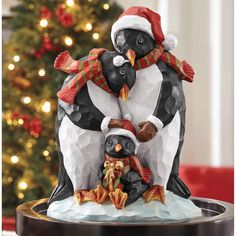 three penguin figurines sitting on top of a table next to a christmas tree