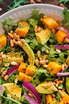 a salad with avocado, carrots, and pine nuts in a white bowl