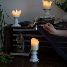 a person is holding a lit candle in front of some books on a table with flowers