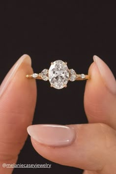 a woman's hand holding an engagement ring with three stones on it, and the middle