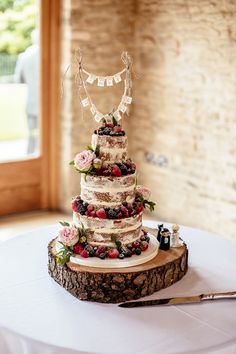 a wedding cake sitting on top of a wooden slice with berries and flowers around it