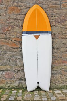 an orange and white surfboard leaning against a stone wall