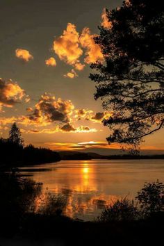 the sun is setting over a lake with clouds in the sky and trees around it