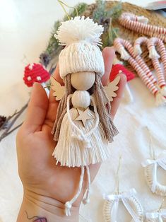 a hand holding a small white doll with tassels on it's head