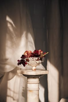 a bowl filled with fruit sitting on top of a white table next to a curtain