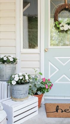 two potted plants are sitting on the front porch next to a welcome mat and door