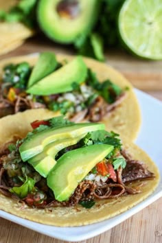 two tacos with meat, avocado and cilantro on them sitting on a plate