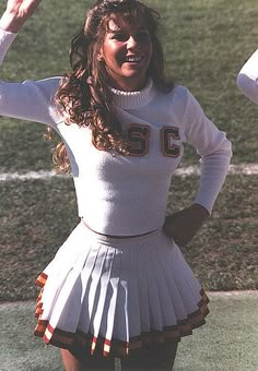 a woman in a cheerleader outfit standing on a field with her hands up to the side