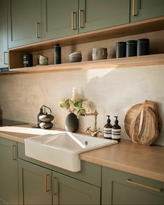 a kitchen with green cabinets and wooden counter tops is pictured in this image, there are vases on the shelf above the sink