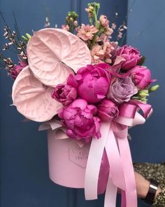 a bouquet of flowers in a pink bucket with ribbon tied around the bottom and leaves on top