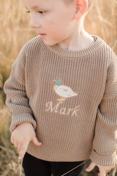 a little boy that is standing in the grass with a bird on it's sweater