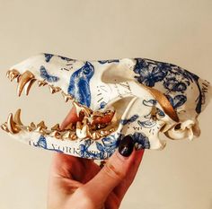 a hand holding a fake animal skull in it's right hand, with blue and white designs