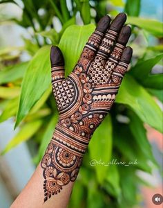 a woman's hand with henna tattoos on it and green leaves in the background