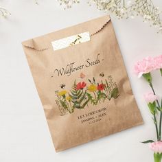 a brown paper bag with wildflower seeds on it next to pink carnations